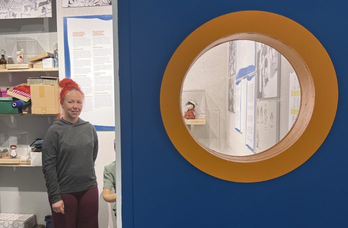 Naantalin museoamanuenssi Mari Termonen ja pyöreästä ikkunasta pilkistävä Hemulin täti -hahmo (Irmeli Metsolan kokoelma). Kaiken kaikkiaan Hemulin täti -nukkeja on näyttelyssä neljä – jokainen keskenään erilaisia.