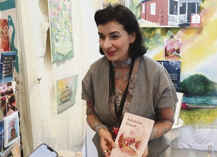 Sibel Kantola Taikamokin tarinat Turun Kirjamessut lokakuu 2026 web Lokakuun alussa järjestetyillä Turun Kirjamessuilla saattoi kohdata kaarinalaisen Mökki Gallerian Sibel Kantolan, joka juhlisti Taikamökin tarinat -teoksen toista painosta. ”Kaikki kirjan tarinat ovat täysin totta – asiat vain sattuvat olemaan luonnostaan erikoisia ja taianomaisia.” hän sanoi. Seuraavaksi tunnelmallisessa mökissä suunnataan katseet tulevaisuuteen suosittujen keskusteluiltojen merkeissä. Kuva: Ragip Önsoy.